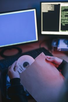 CD being inserted into a sleeve near computer displays with coding interface.