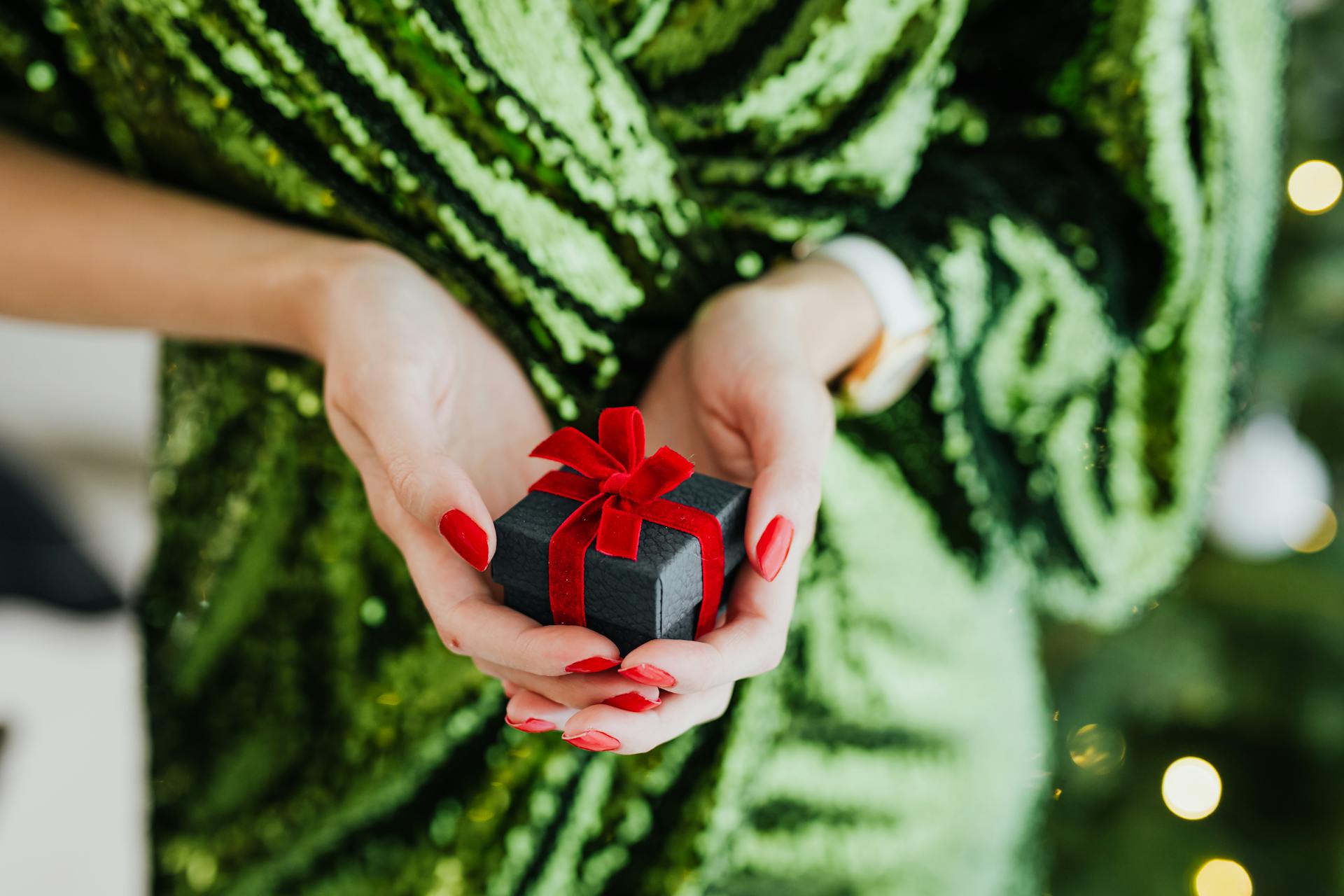 Close-up of woman holding a black gift box with a red bow against a festive background.