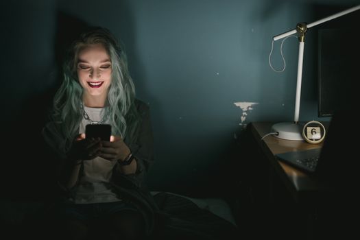 昏暗的房间里，屏幕的光照亮了一名对着智能手机微笑的年轻女子