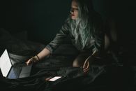 一位女士在黑暗而舒适的房间里，用笔记本电脑和智能手机工作，屏幕的光照亮了房间