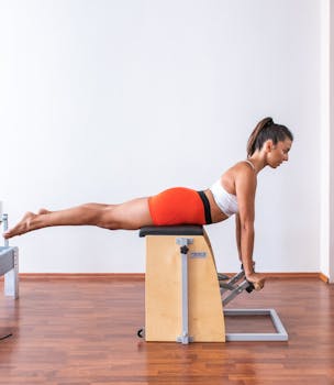 A woman performs a Pilates exercise on a Wunda chair, showcasing strength and balance.