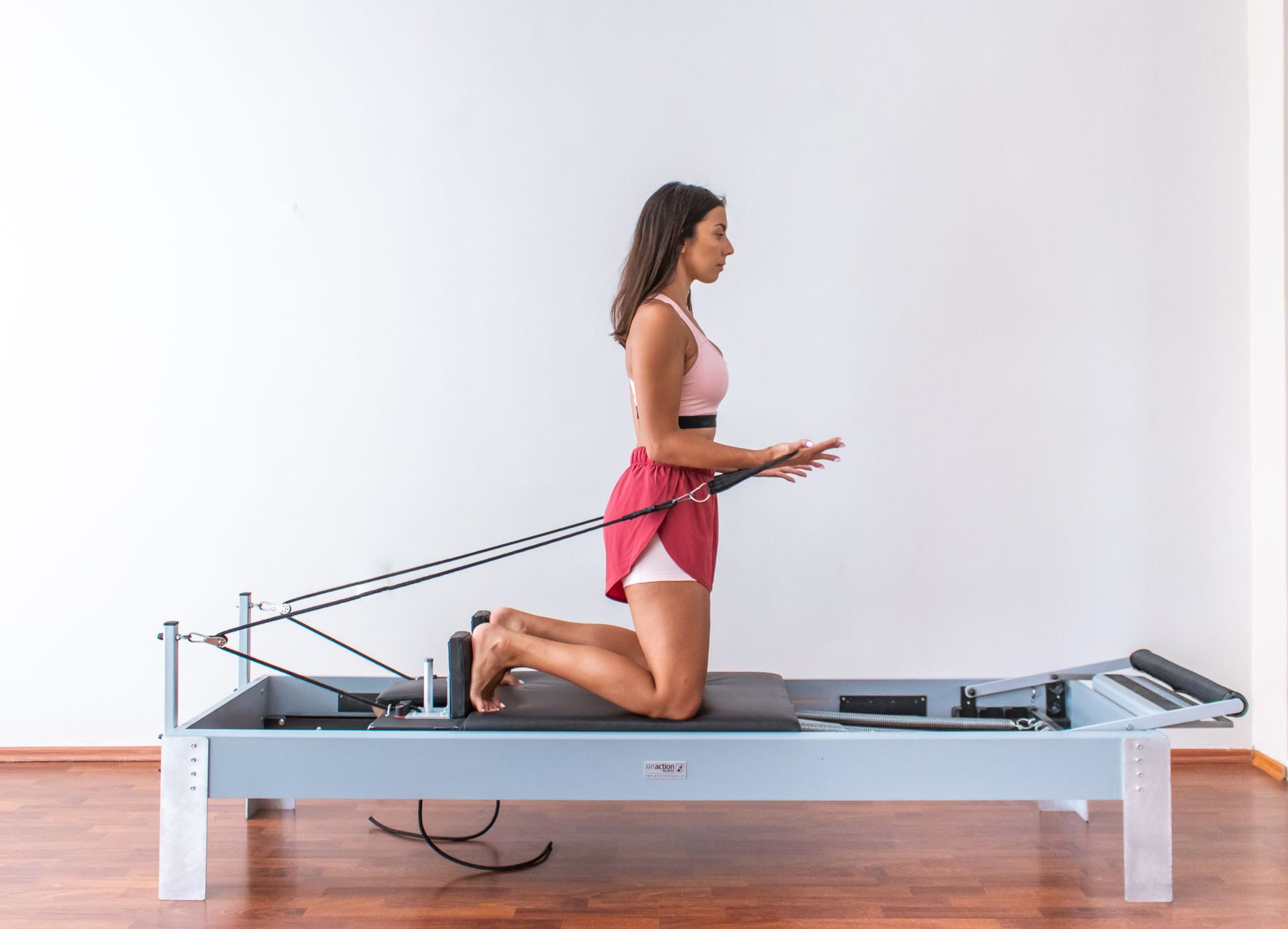 Side view of a woman in activewear exercising on a pilates reformer indoors.