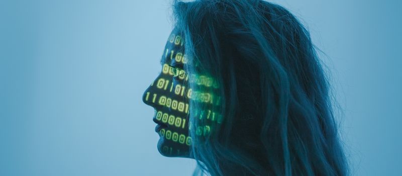 AI技術の進化を象徴する、顔にバイナリコードが投影された女性のシルエット画像。グローバルなAI投資拡大のイメージ。