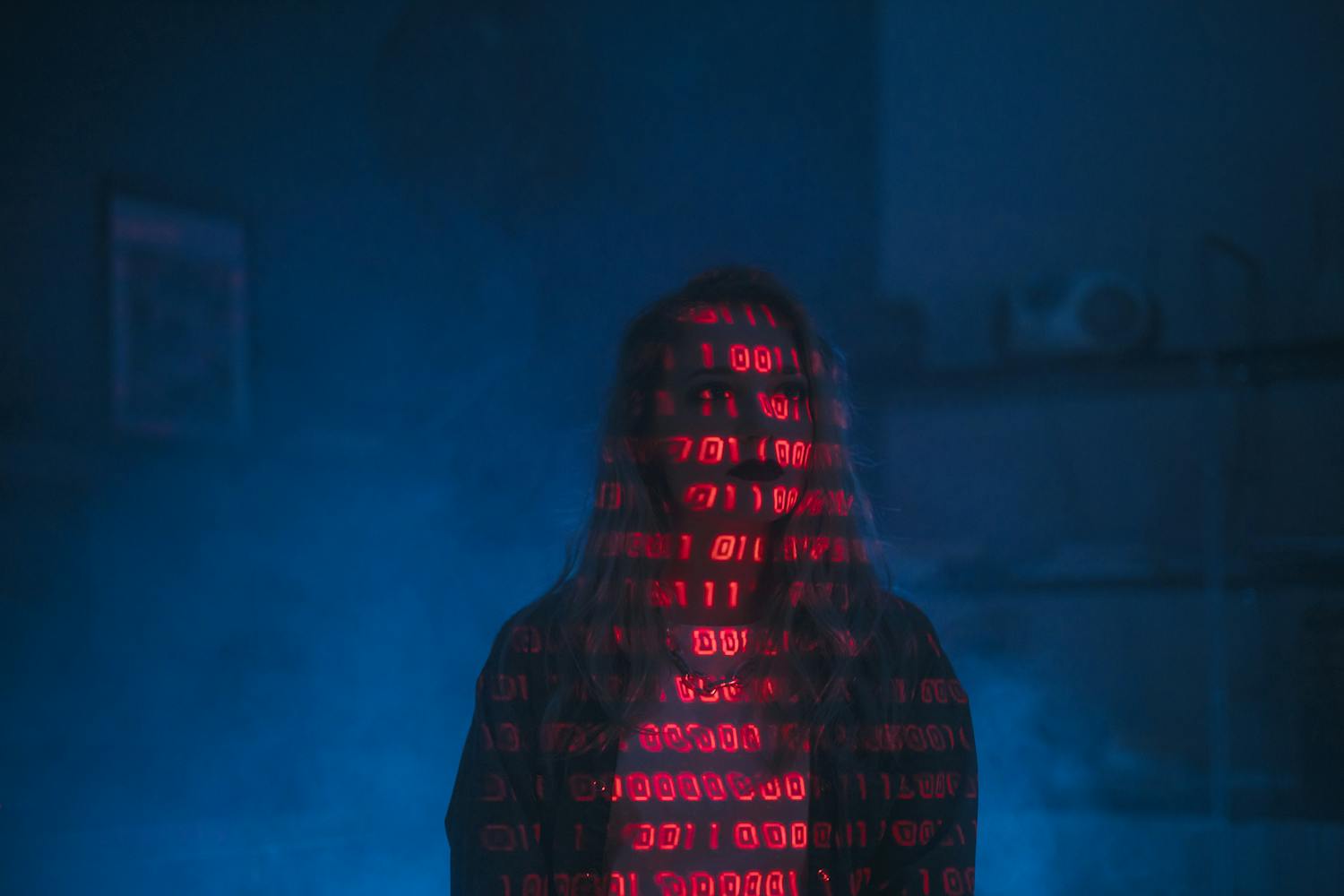 A mysterious silhouette with red binary code projected over the face, set against a dark, moody background.