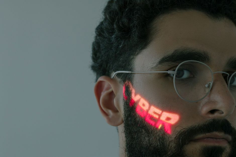 Close-up of a bearded man wearing eyeglasses with 'CYBER' text projected on his face.