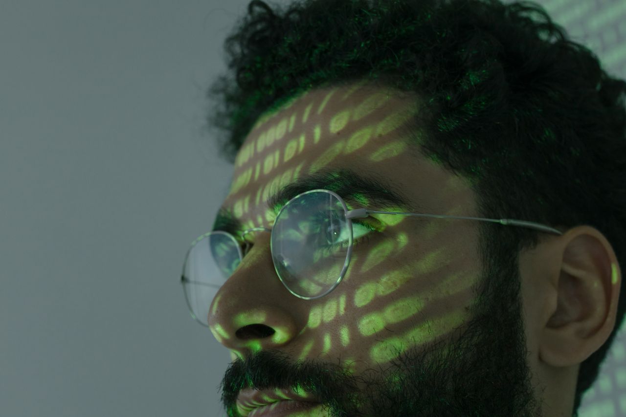 a man wearing glasses with binary code projected across his face symbo