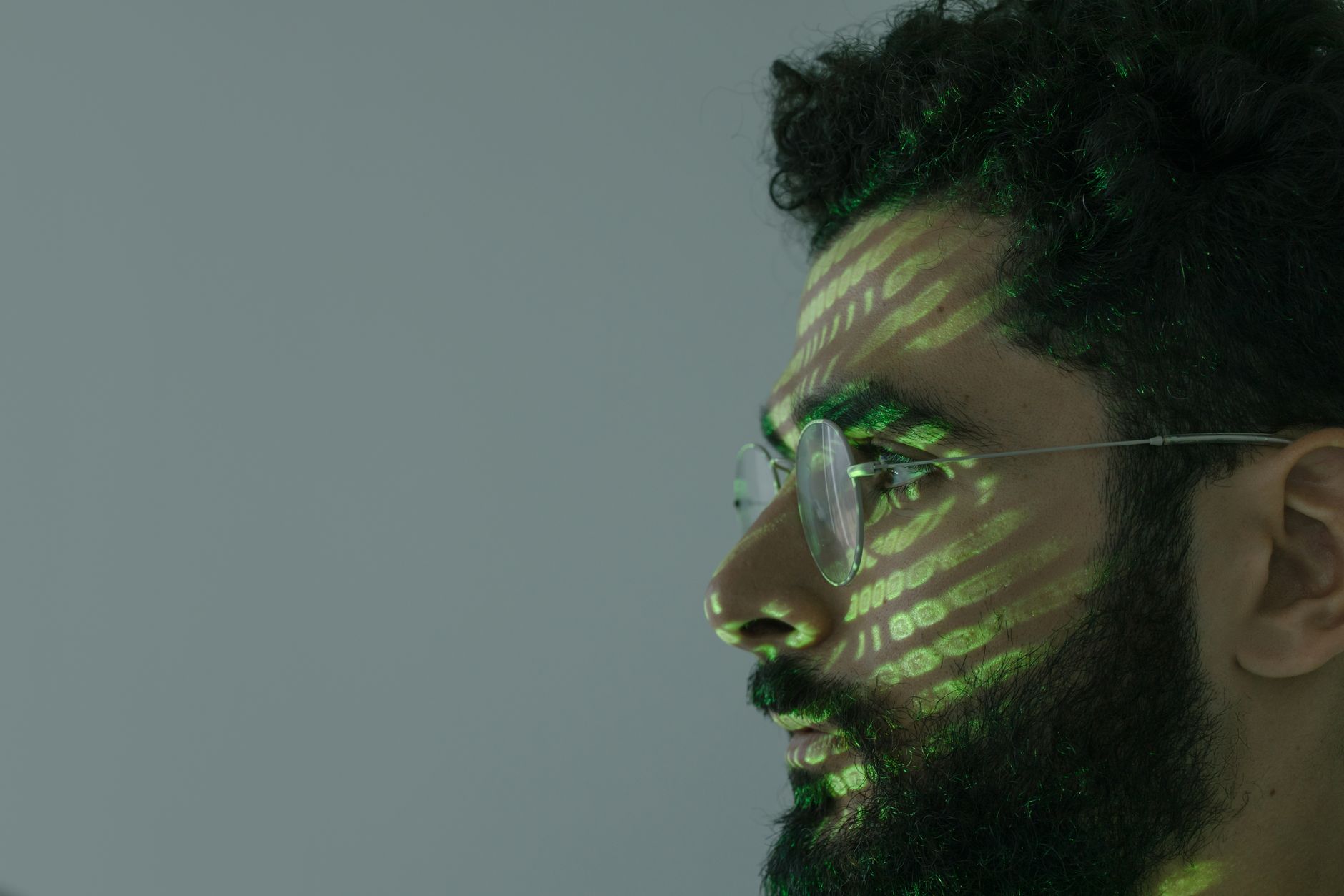 Side profile of a man with eyeglasses and green binary code projected on face.