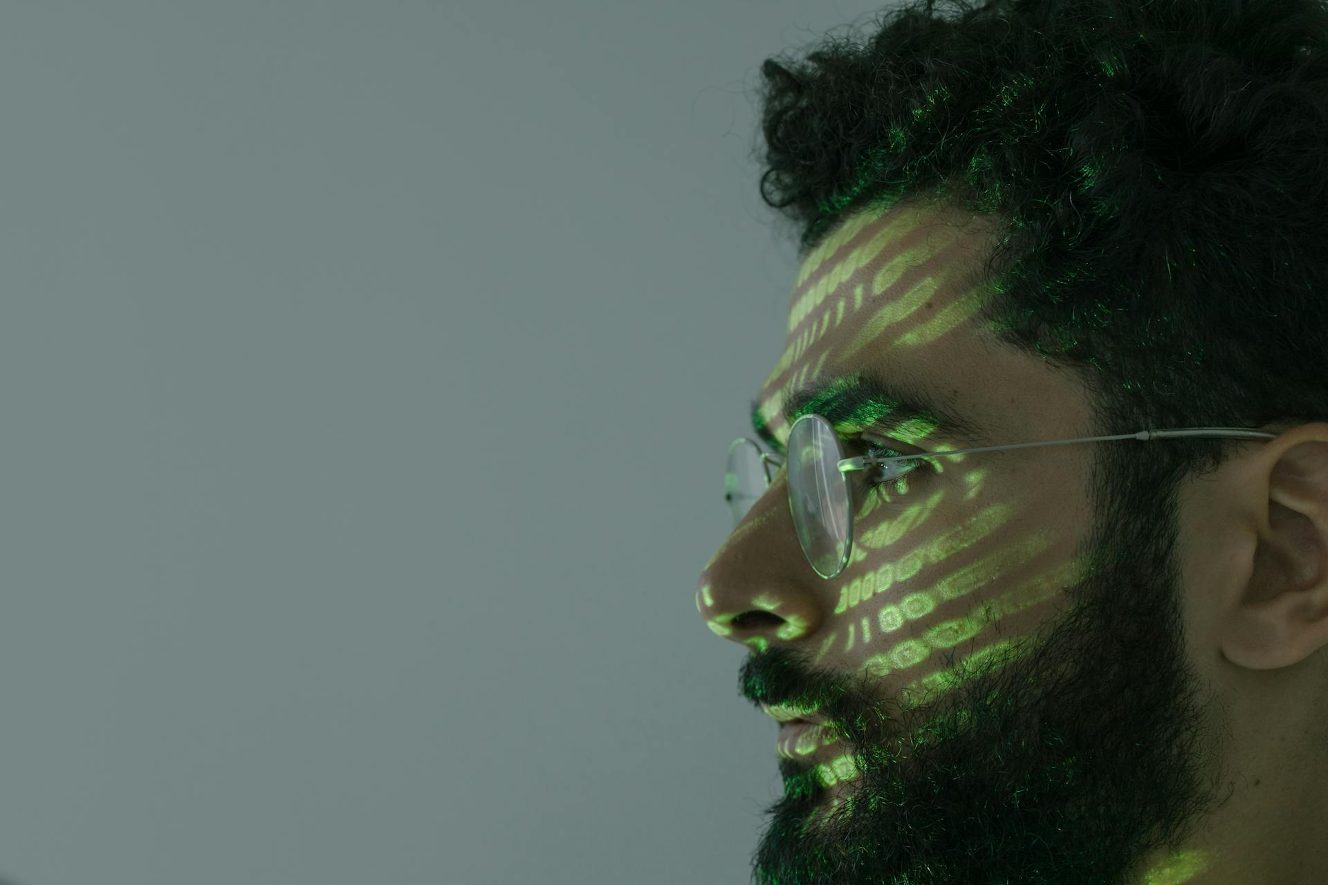 Side profile of a man with eyeglasses and green binary code projected on face.