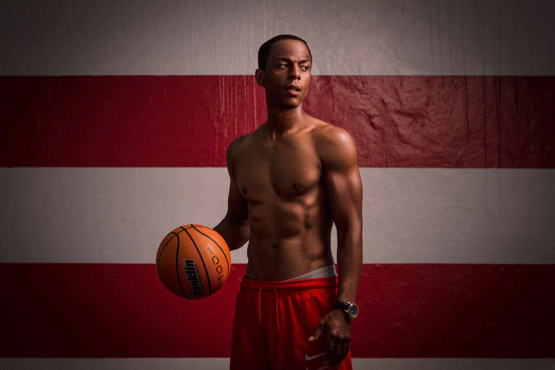 A fit male athlete is holding a basketball indoors, showcasing strength and focus.
