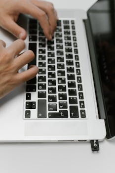 Hands typing on a silver laptop keyboard, showcasing digital interaction with technology.