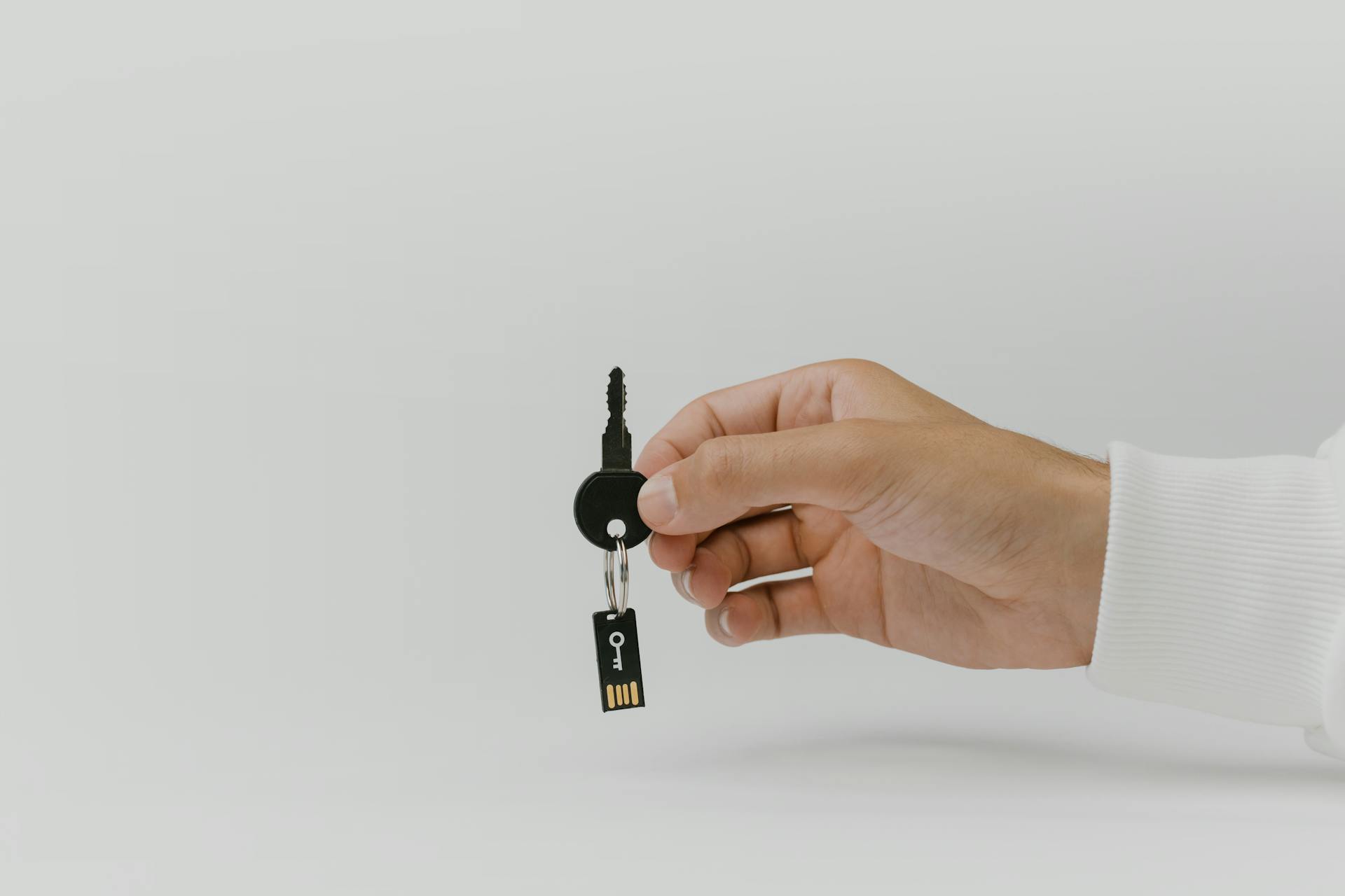 Hand holding keychain with integrated USB flash drive against a plain background.