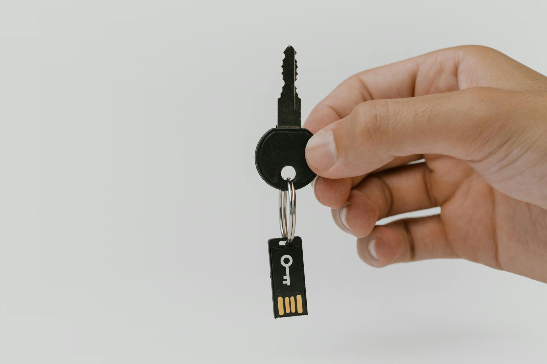 A close-up of a hand holding a key with an attached USB drive, highlighting security and technology.