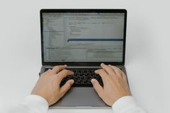 Two hands resting on a laptop keyboard seen from above on a white desk