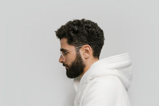 Side view of a bearded man with eyeglasses, wearing a white hoodie. Minimalist background.