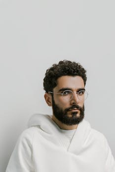 一名男子的特写肖像，他卷发、戴眼镜，穿着白色连帽衫