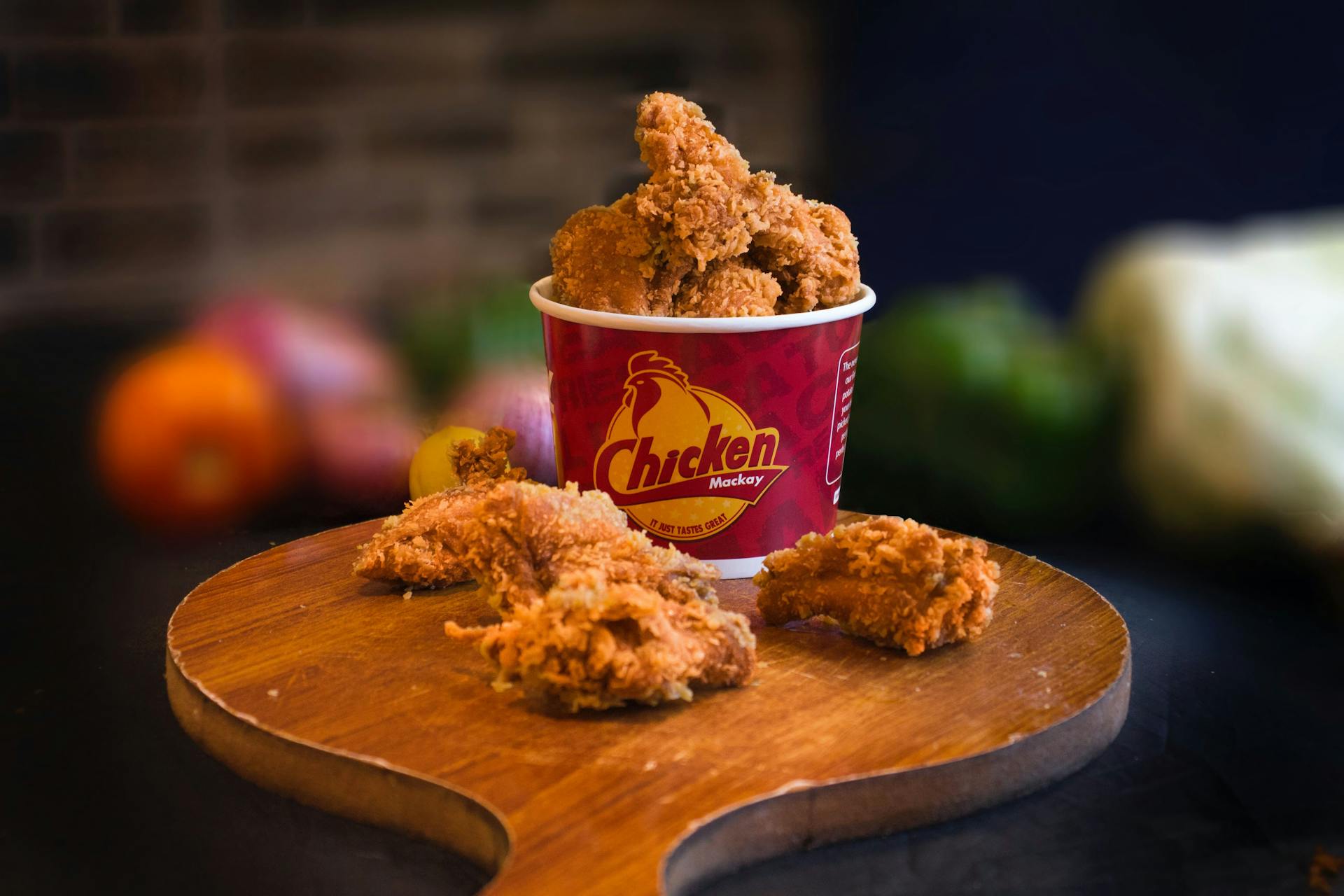 Mouth-watering fried chicken in a bucket displayed beautifully with blurred vegetables in the background.