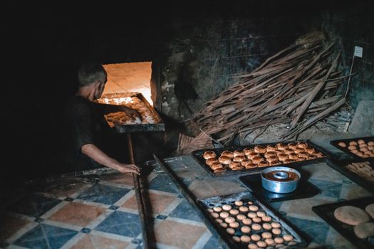 A Moroccan baker skillfully bakes bread in a traditional wood-fired oven.