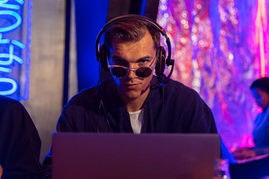 Focused man in headphones and sunglasses uses laptop in vibrant studio setting.