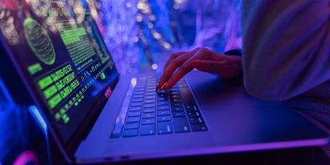 Close-up of hands typing on a laptop displaying cybersecurity graphics, illuminated by purple light.