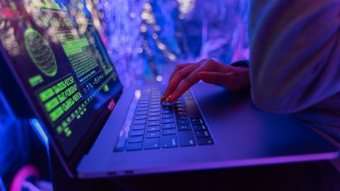 Close-up of hands typing on a laptop displaying cybersecurity graphics, illuminated by purple light.