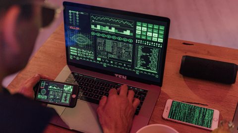 Man working with cybersecurity software on laptop and smartphone.
