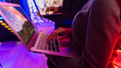 Two professionals analyzing data on laptops with colorful lighting, focusing on cybersecurity details.