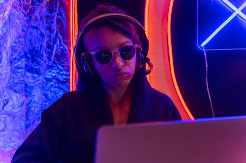 Free Person in sunglasses and headphones using a laptop in a neon-lit setting. Stock Photo