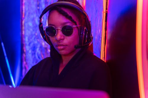 Free A portrait of a woman wearing sunglasses and a headset, bathed in neon pink and blue lighting. Stock Photo