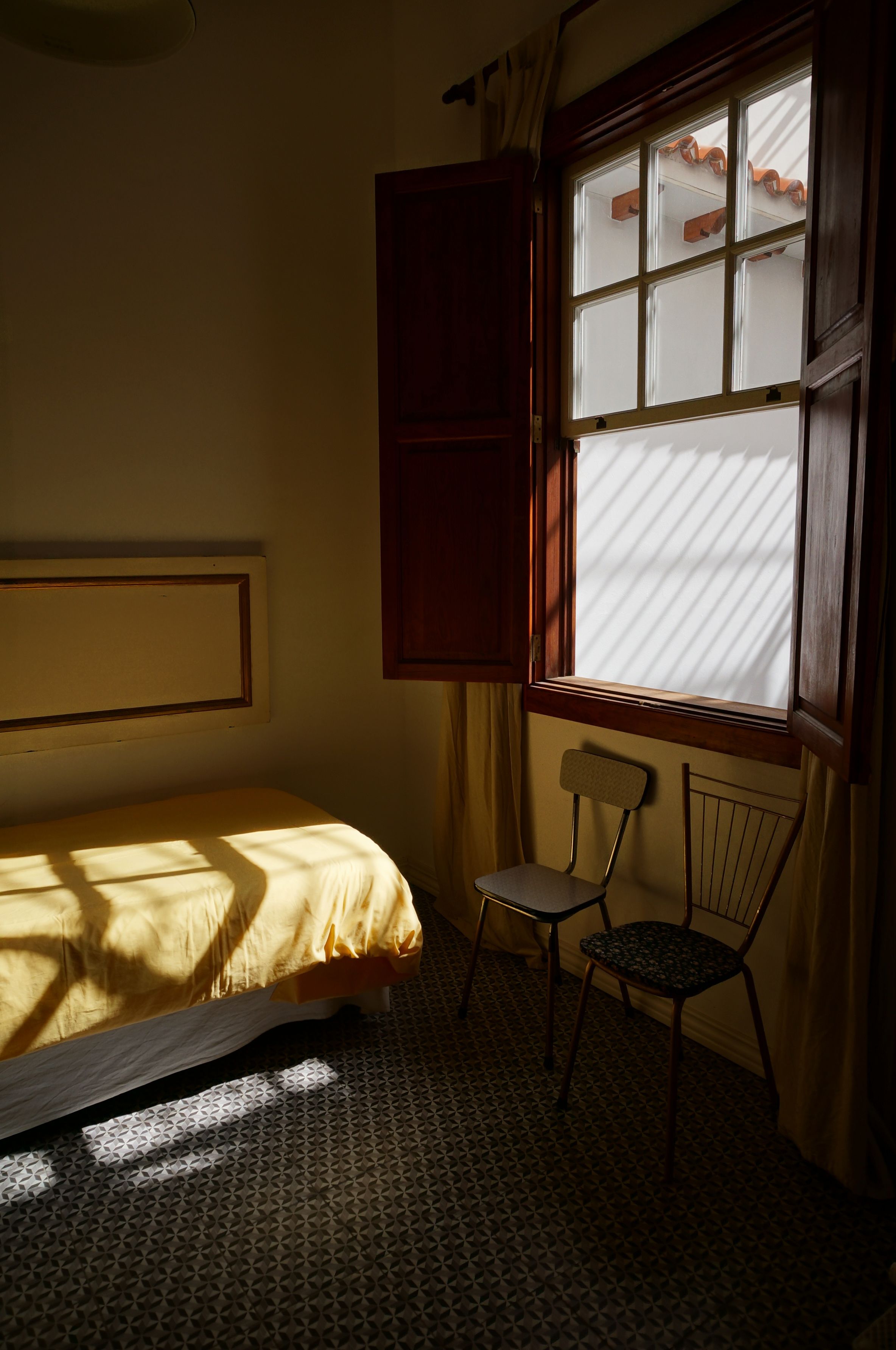 A guest bedroom with morning light coming through the shutters
