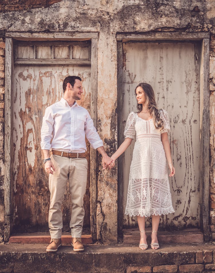 Happy Couple In Stylish Apparel Holding Hands Near Old Building