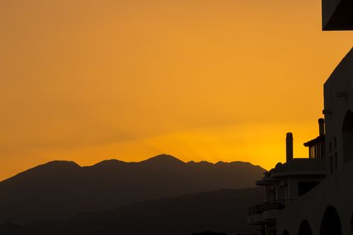 Free A breathtaking golden sunset view over the silhouettes of mountains and buildings in Rethymno, Greece. Stock Photo