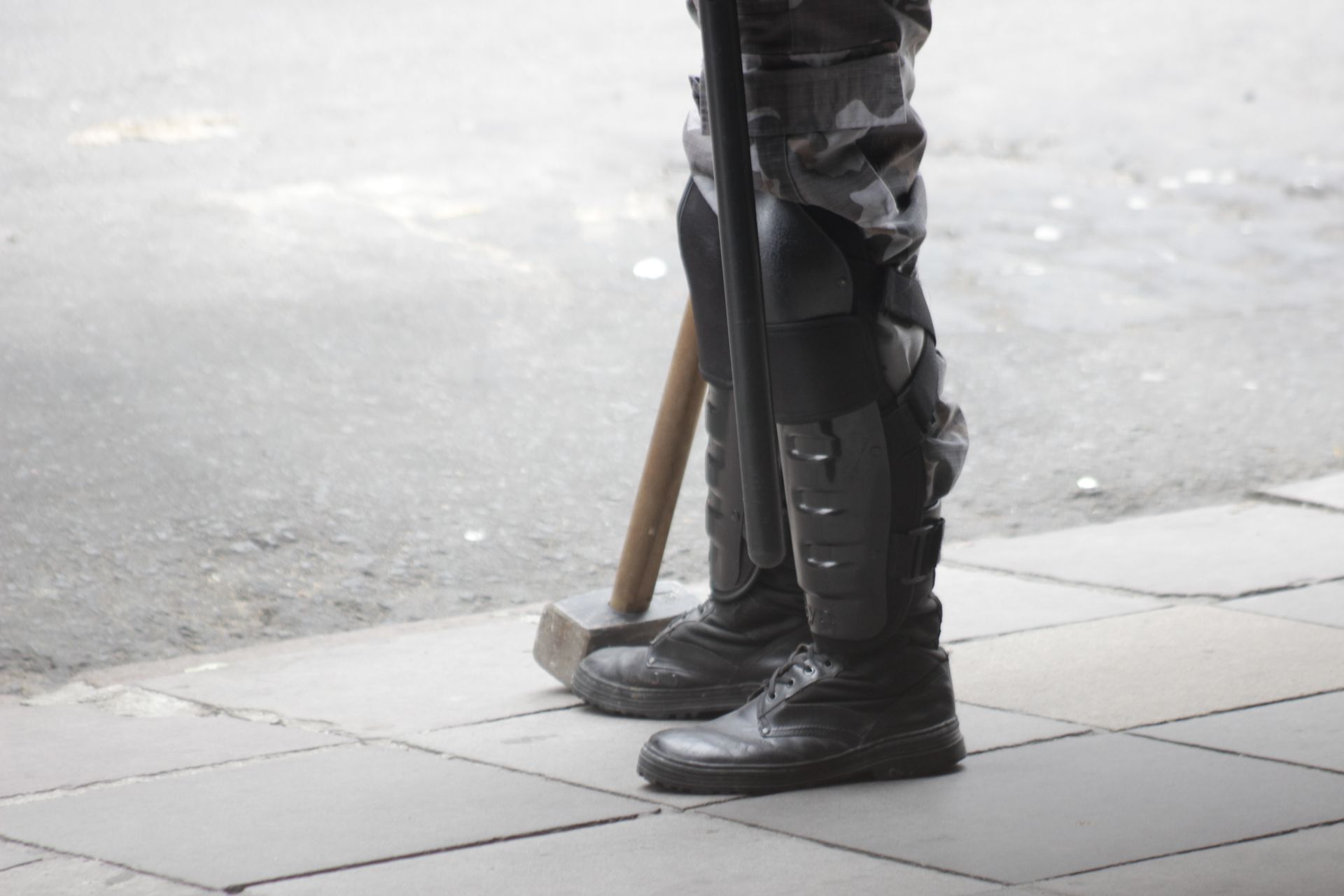 Detailed view of a person standing in protective riot gear and boots on a sidewalk.