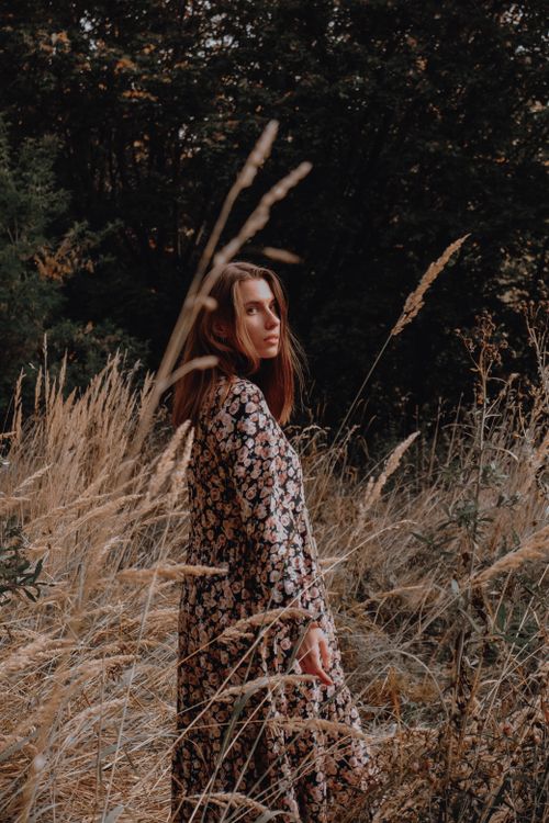 Free Serious pensive female looking at camera and promenading in meadow of high grass and trees Stock Photo