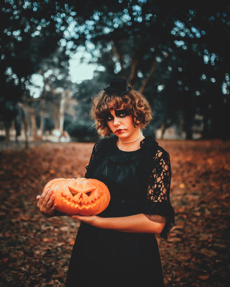 Woman With Halloween Makeup And Carved Pumpkin In Park