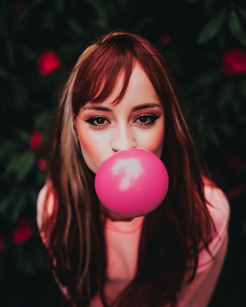 Young female in trendy apparel blowing pink chewing gum while looking at camera