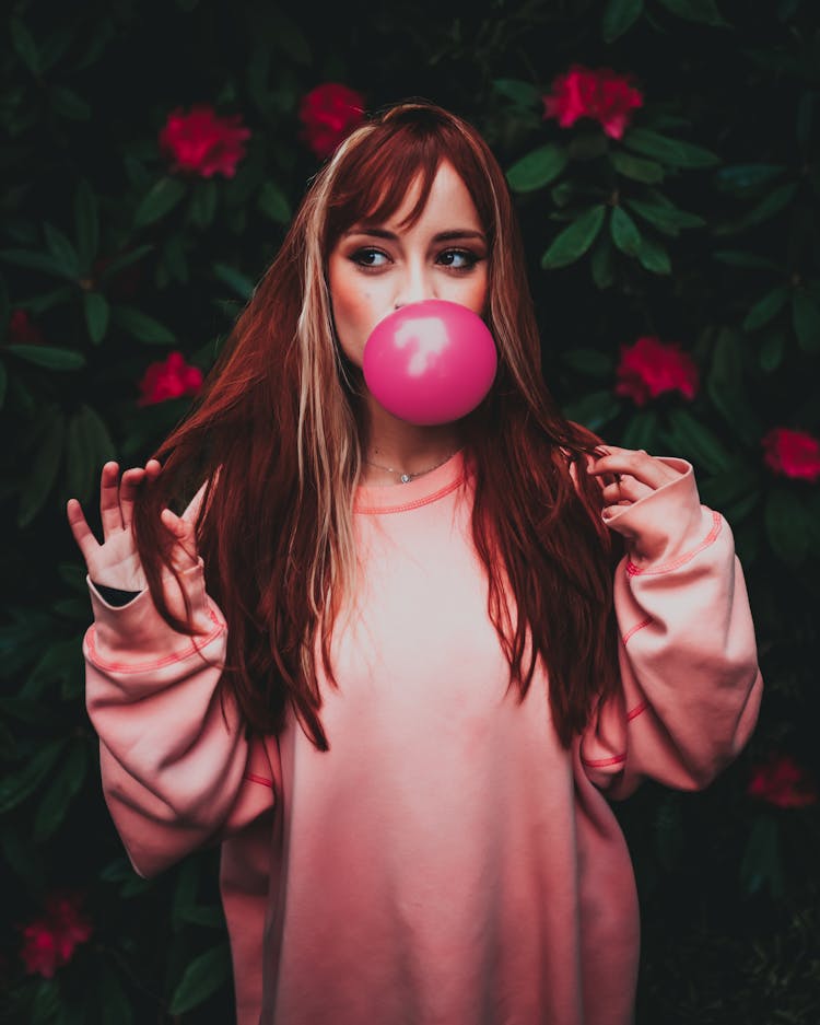 Dreamy Woman In Trendy Clothes Blowing Pink Gum In Garden