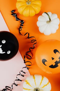 Halloween-themed flat lay with pumpkins and spooky balloons on orange and pink background.