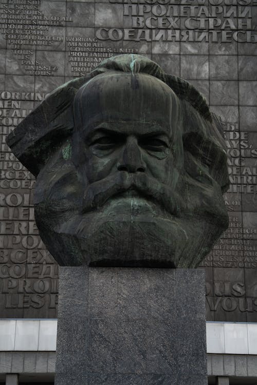 Stone head sculpture of revolutionary placed on high postament against stone wall in city
