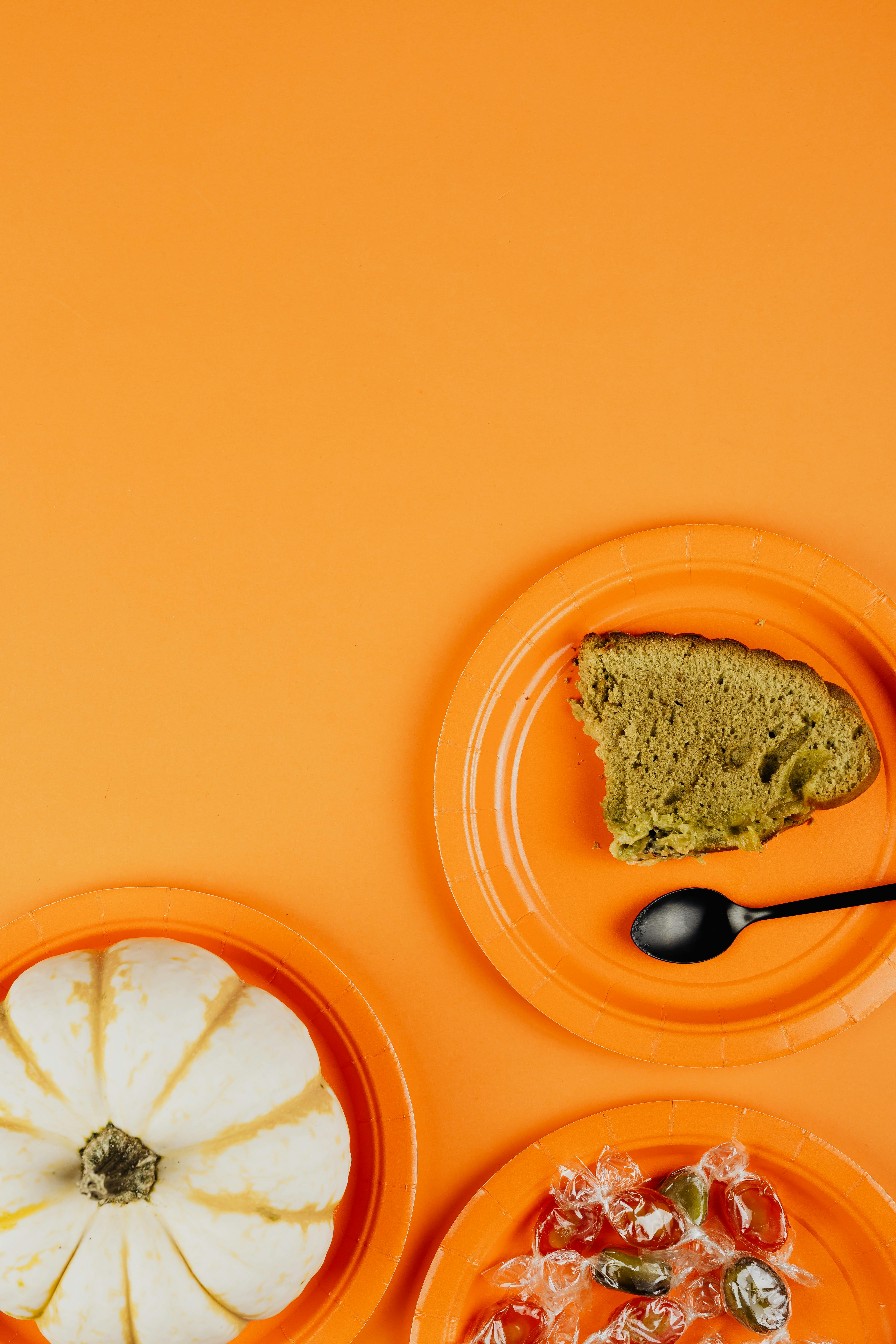 橙色的盘子上摆放着南瓜和蛋糕片，搭配着糖果，背景也是橙色，营造出秋天的氛围