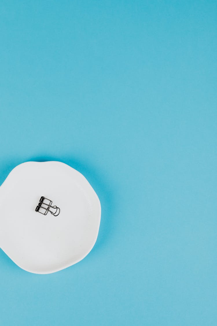 One Paperclip On A White Plate On Blue Background 