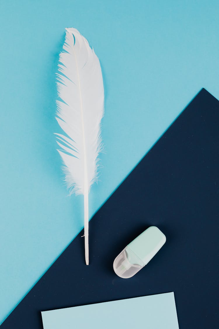 White Feather And A Highlighter On Blue Paper 