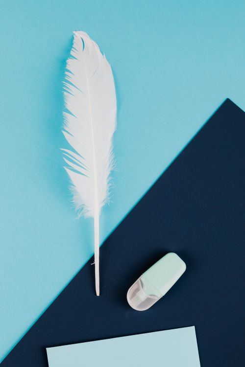 Free A top view of a white feather and an eraser on blue paper, showcasing simplicity and creativity. Stock Photo