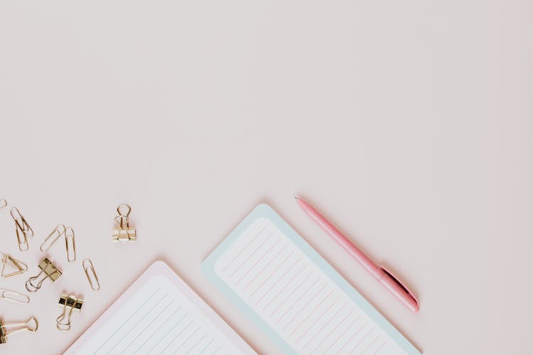 Pink Pen, Notebook And Paper Clips On White Background