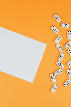 橙色背景上，多米诺骨牌以极简主义风格排列，上方有一张空白的白纸