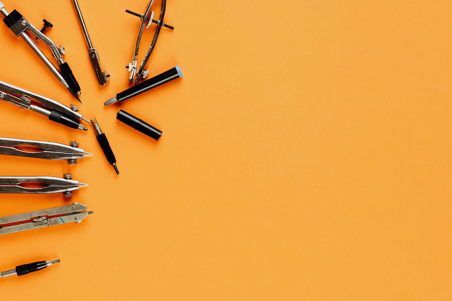 Top view of various drawing tools and compasses on an orange background with copy space.