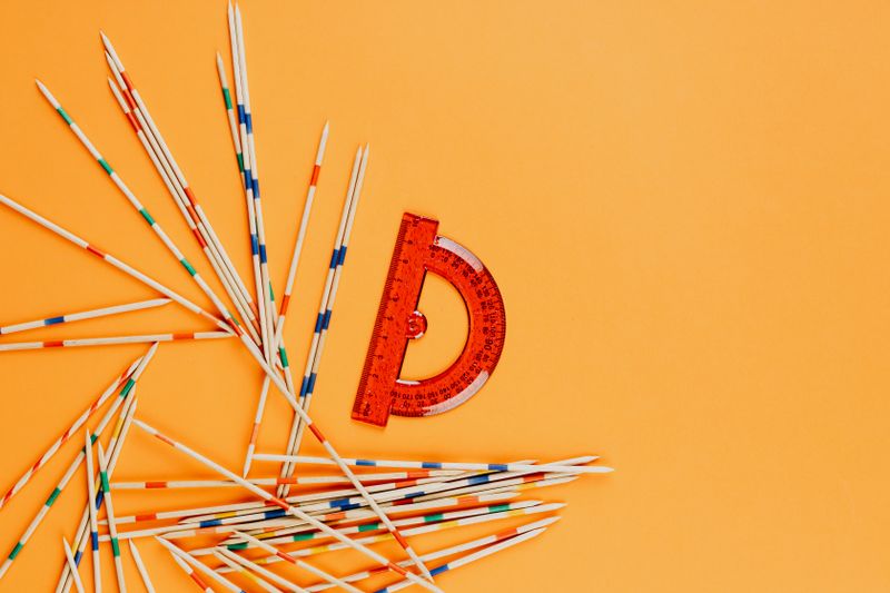 A vibrant arrangement of a red protractor and colorful striped sticks scattered on an orange background.
