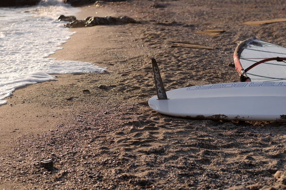 Surfboard lying on a serene Greek beach shore during a sunny morning, capturing the essence of a quiet vacation spot.