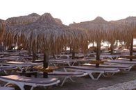 Serene view of straw umbrellas and loungers on a Greek beach resort at sunset.