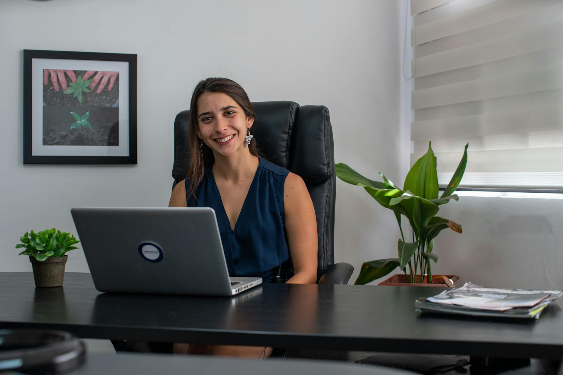 Smiling businesswoman seated at desk with laptop in a modern office.