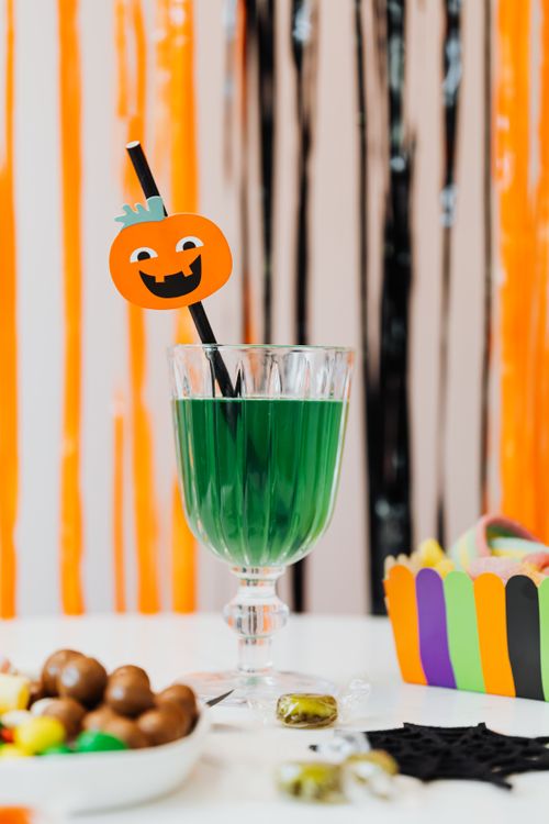 Free Green Halloween cocktail in glass with pumpkin straw on decorated table. Stock Photo